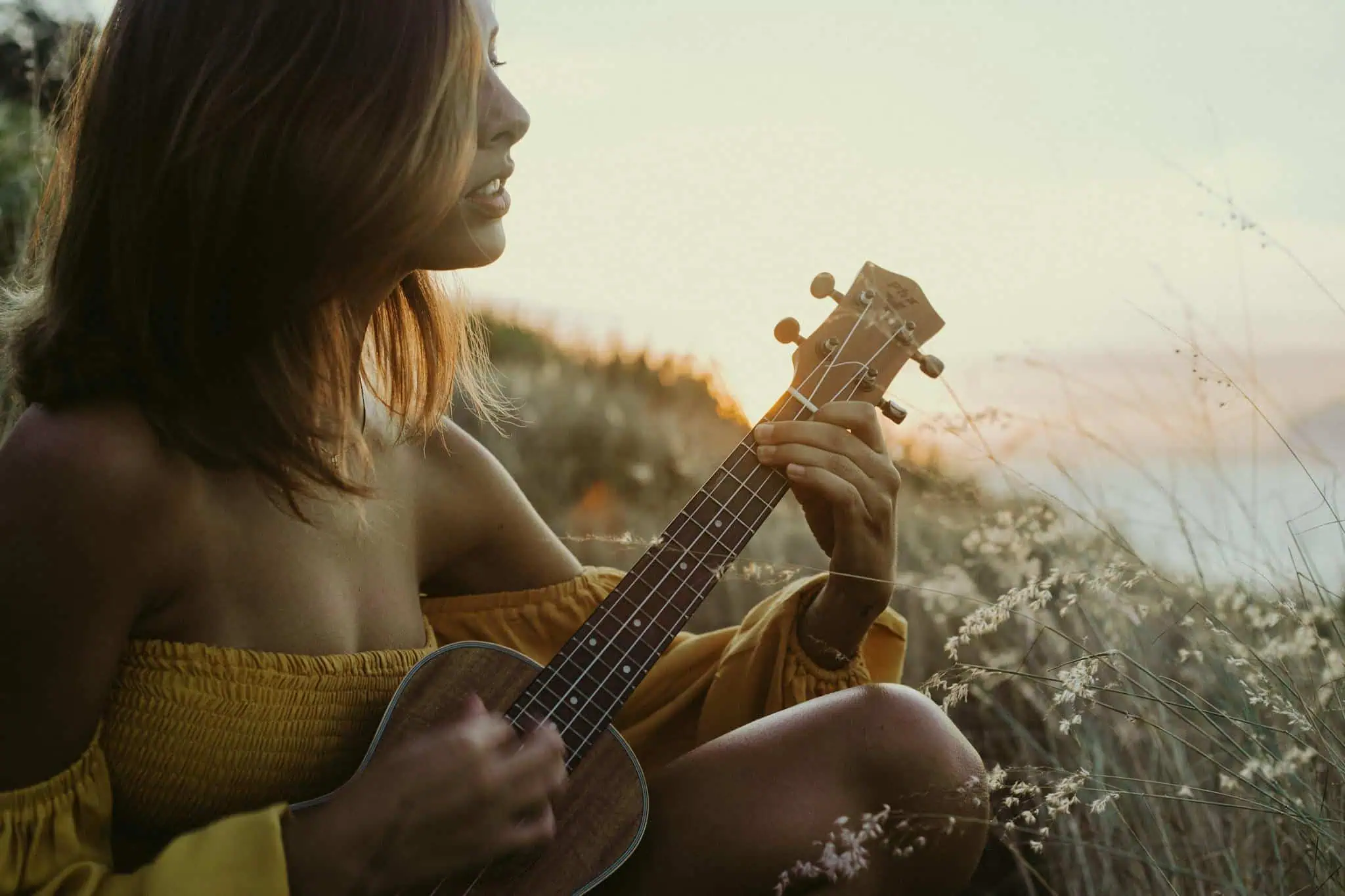 A woman strums a ukulele in a warm sunset meadow, creating a serene musical moment.
