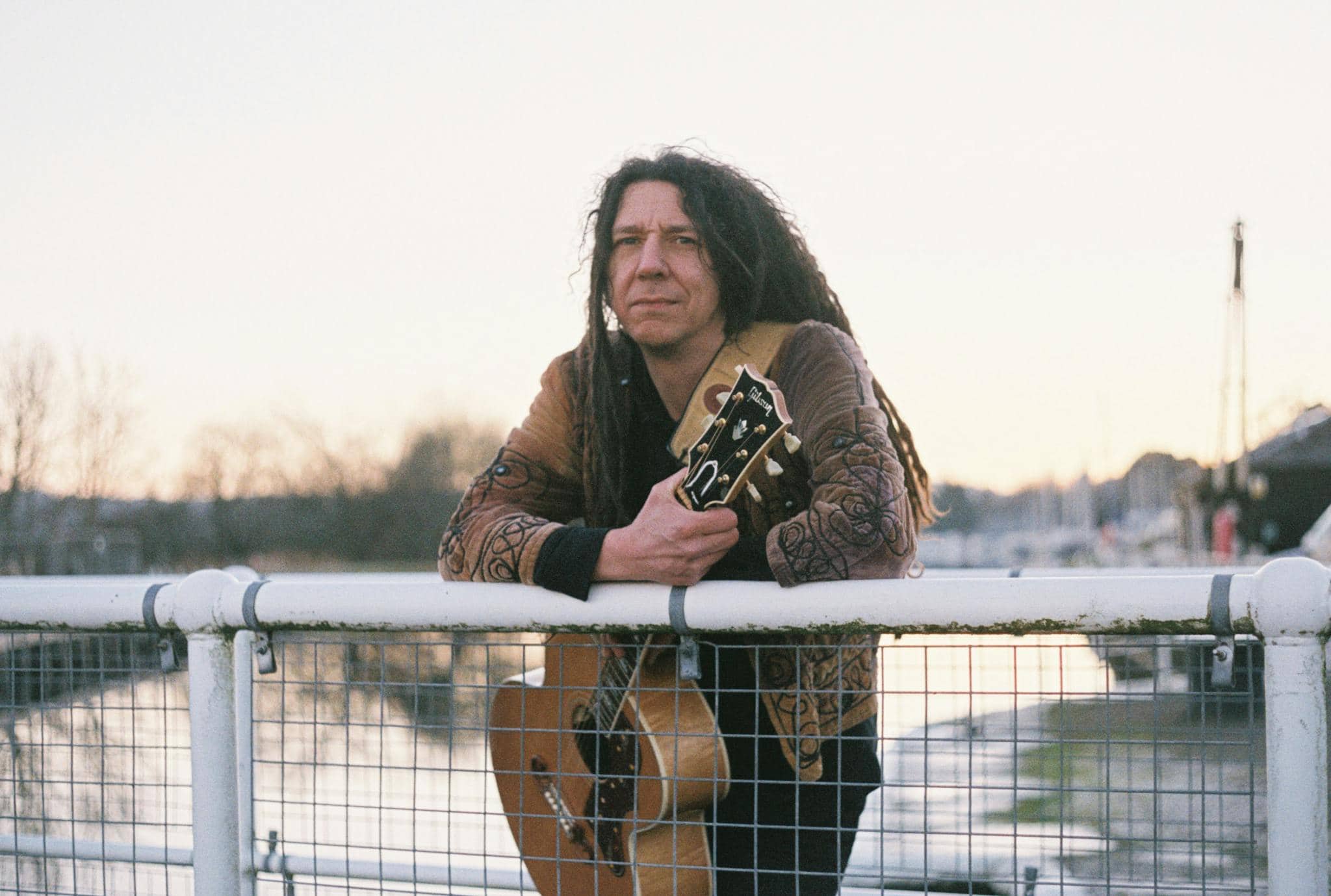 Man with dreadlocks holding acoustic guitar by the canal in Inverness, Scotland.